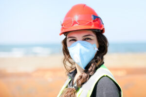 Occupational health and safety (OHS) woman staff (engineer) looking at the camera with protective mask for coronavirus (COVID-19) in the construction field.
